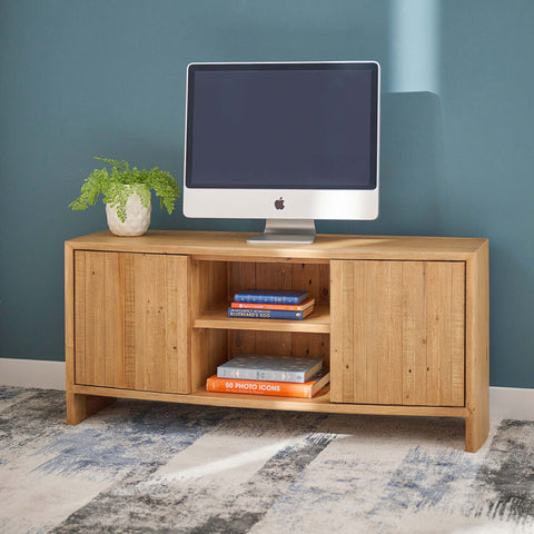 Wooden TV stand with a computer monitor, books, and a plant against a blue wall.