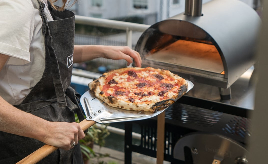 Person holding a pizza out of an outdoor pizza oven.