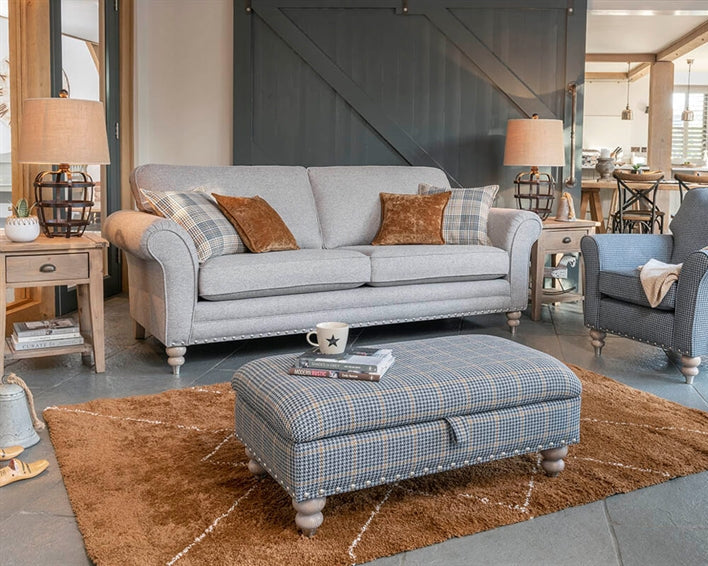 Living room with gray sofa, blue armchair, and patterned ottoman on a brown rug.