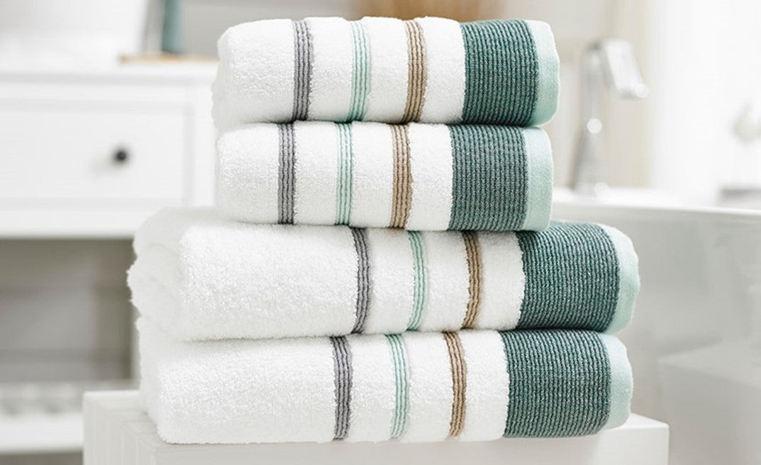 Stack of striped towels on a white table with a blurred bathroom background.