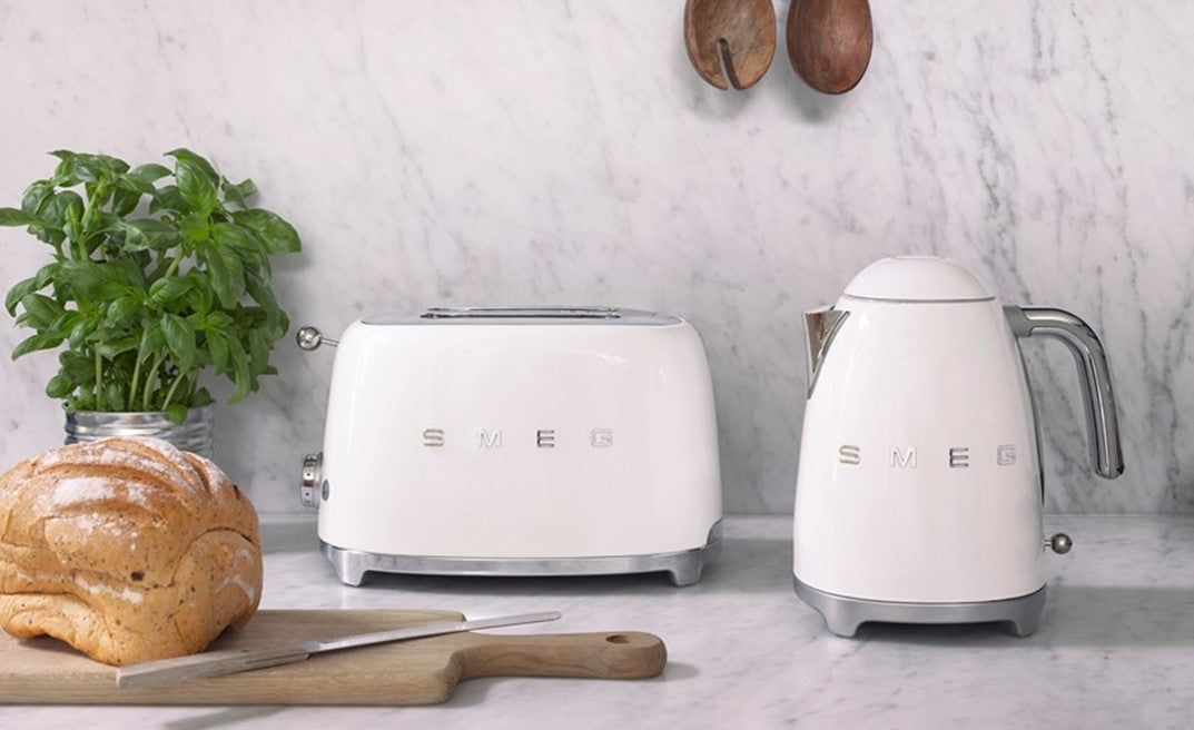 White SMEG toaster and kettle on a kitchen counter with bread on a chopping board.