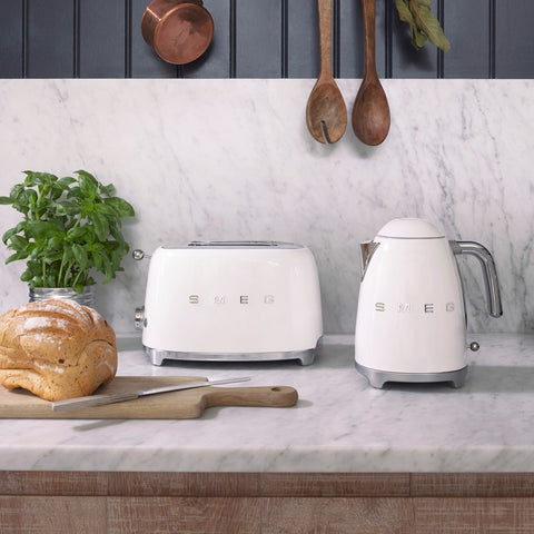 White SMEG toaster and kettle on a kitchen counter with bread on a chopping board.