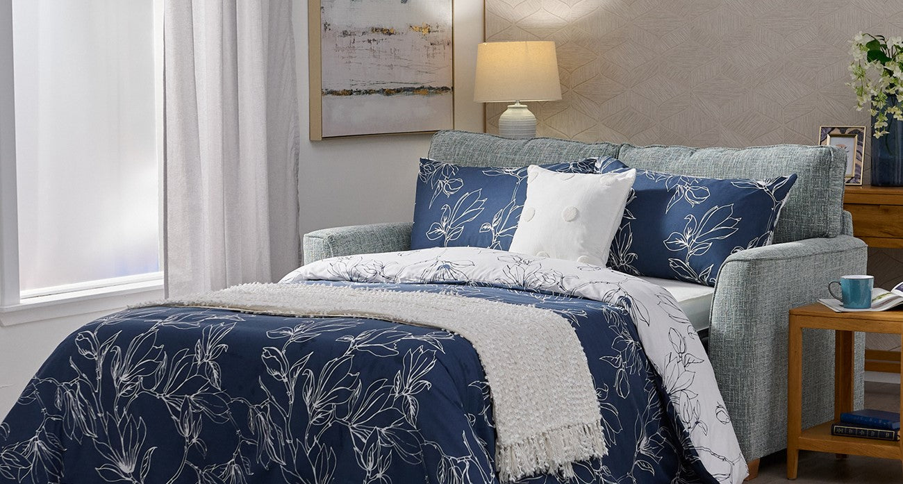 Navy floral comforter on a sofa bed in a living area with a lamp.