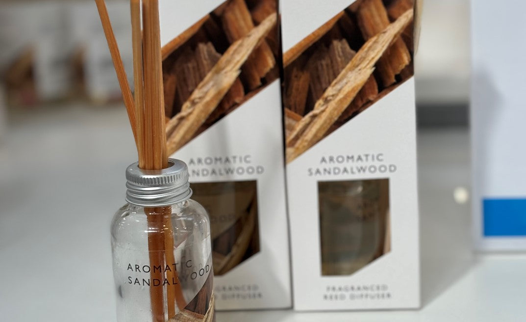 Aromatic sandalwood diffuser with reeds and packaging in the background.