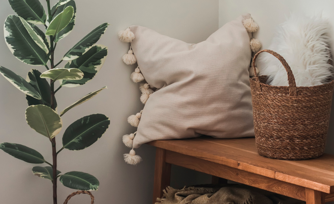 Decorative pillows on a wooden bench next to a plant